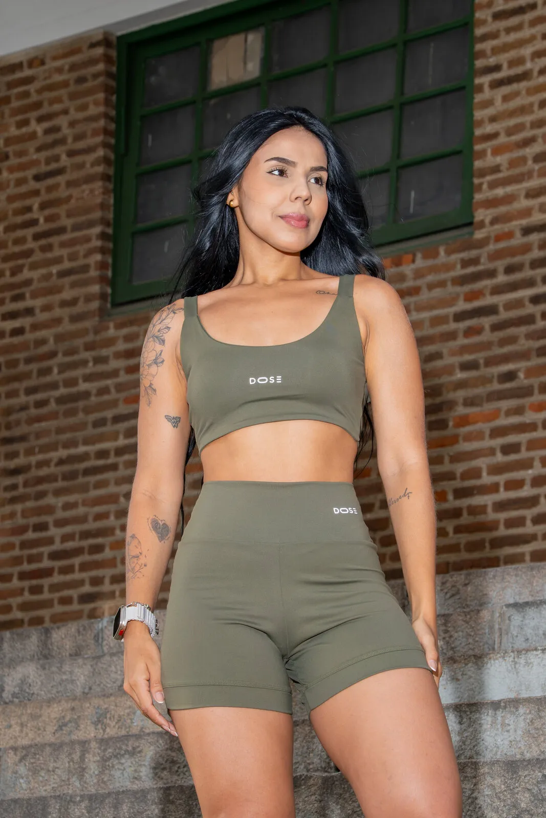 Modelo em frente a um prédio de tijolos com o conjunto de top de alças e shorts, com a assinatura DOSE no top e no shorts.